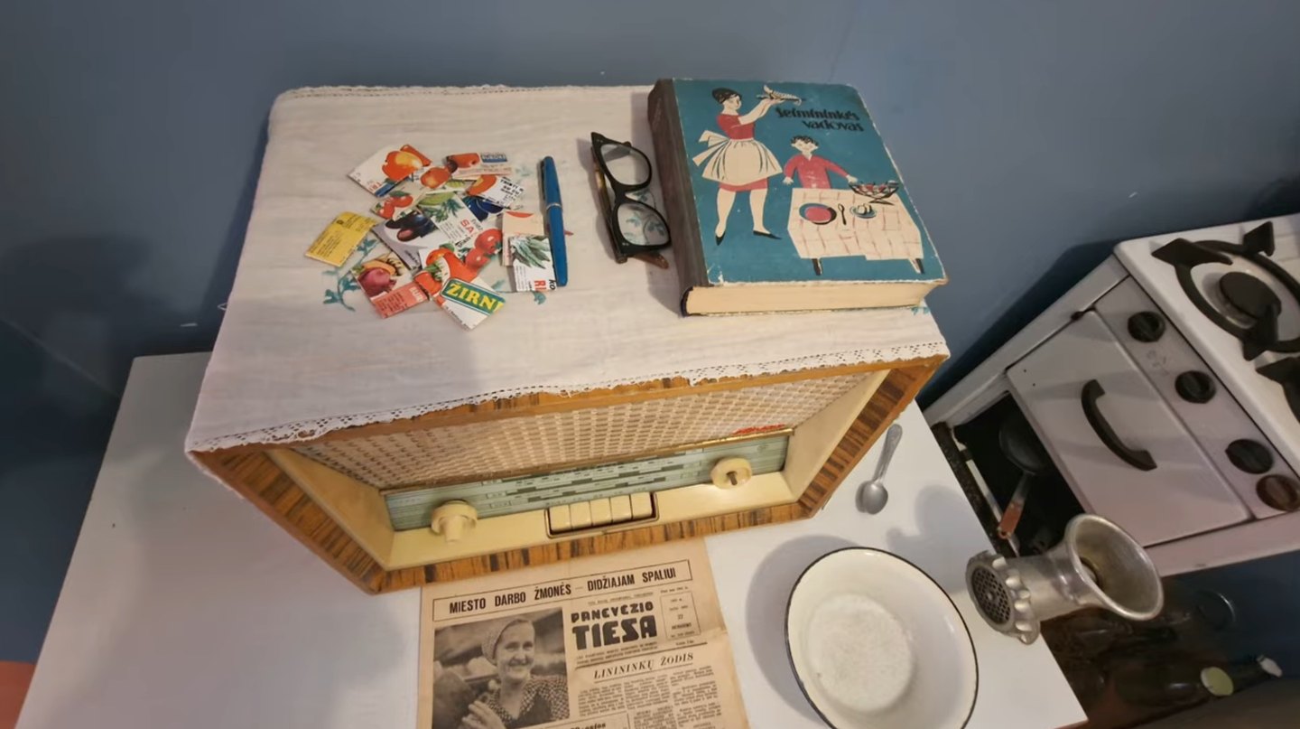 Ekspozycja historii codzienności ze starym radiem, książką kucharską i gazetą w Muzeum Krajoznawczym w Poniewieżu