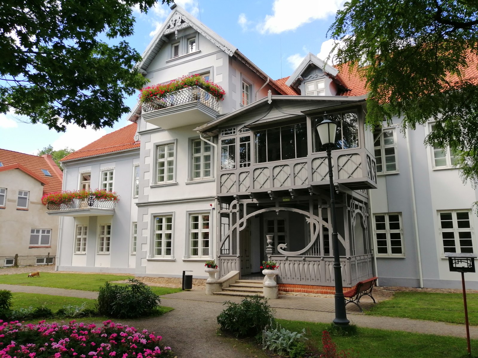 Balkony z kwiatami i drewniana weranda w dworze Hugo Scheu w Šilutė.