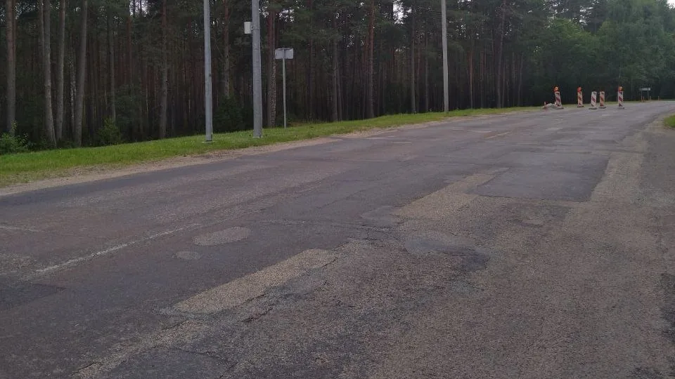 Połatany i nierówny asfalt oraz tymczasowe zapory drogowe na dojeździe do Wisagini